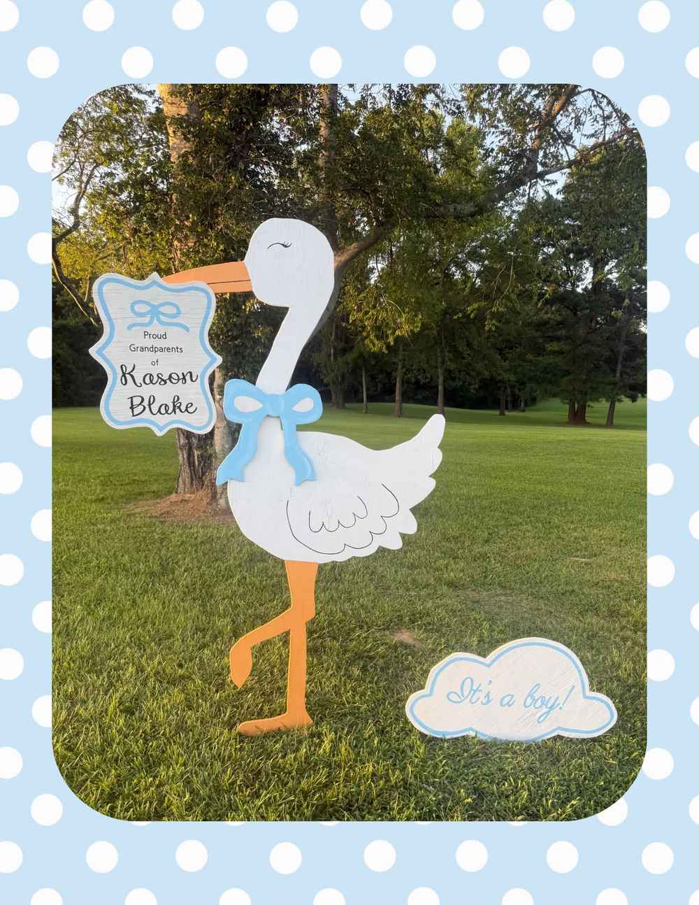 A white wooden boy stork with a blue bow standing in a yard, holding a sign that reads &ldquo;Proud Grandparents of Kason Blake&rdquo; next to an &ldquo;It&rsquo;s a boy!&rdquo; cloud