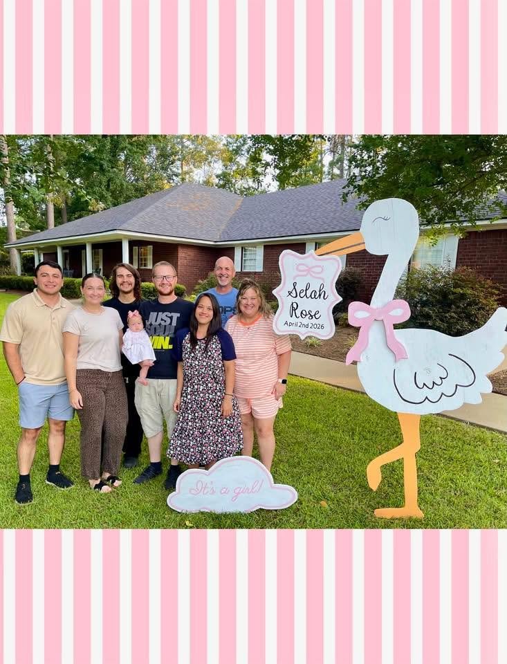Family standing in front of a brick home with a girl stork sign reading &ldquo;Selah Rose, April 2nd 2026&rdquo; and an &ldquo;It&rsquo;s a girl!&rdquo; cloud, holding baby Selah